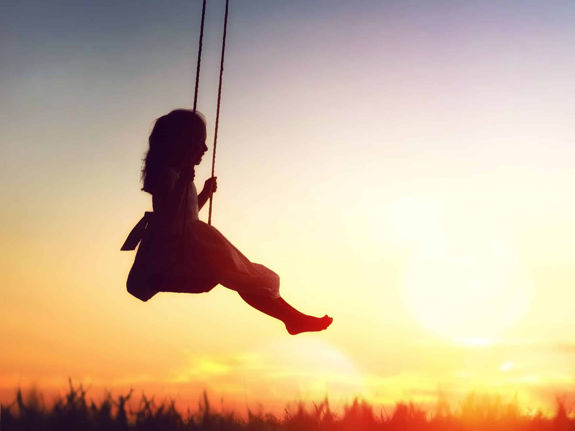 Une fillette sue une balançoire au soleil couchant