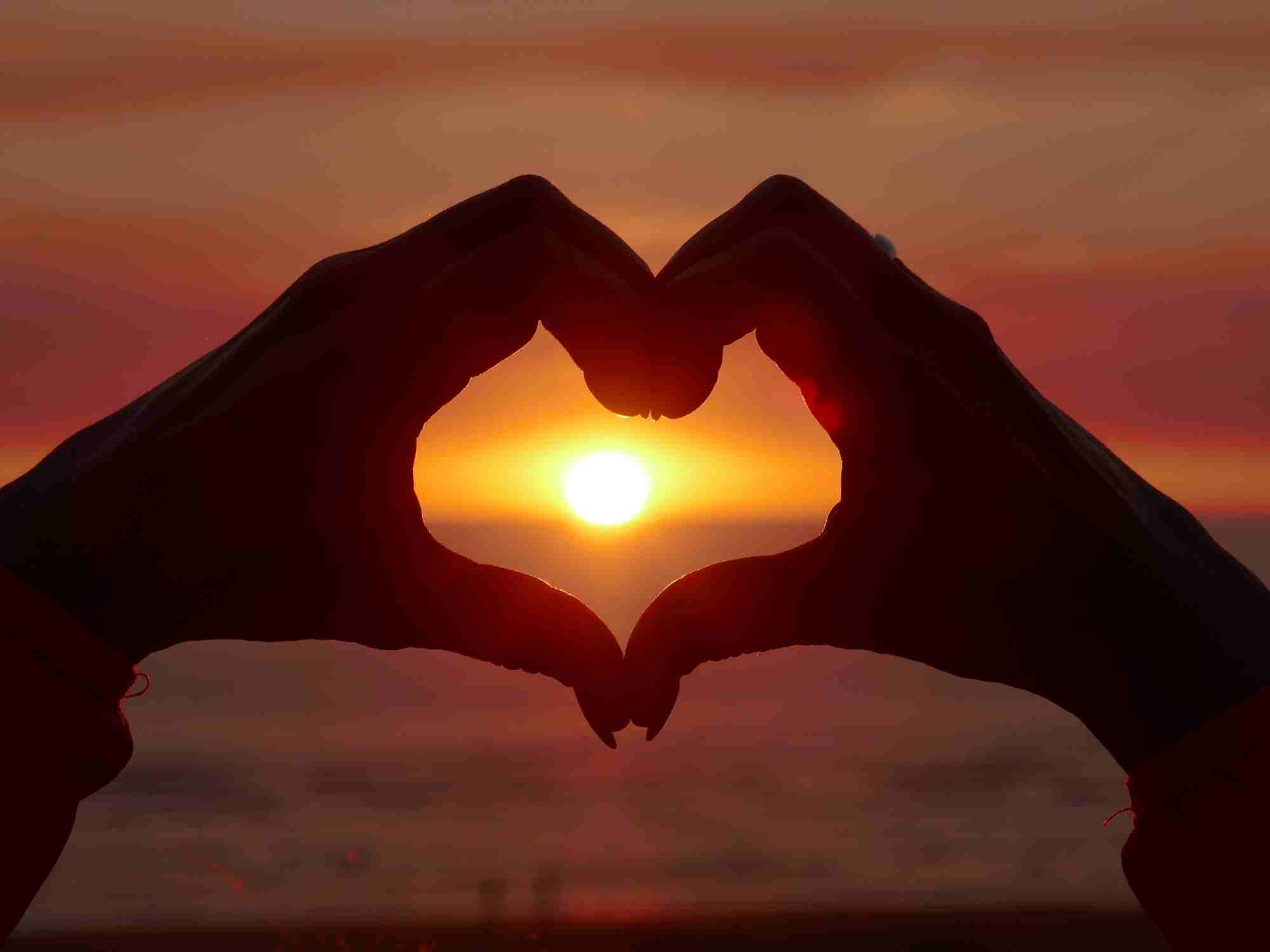 Deux mains forment un coeur dont le centre est le soleil couchant